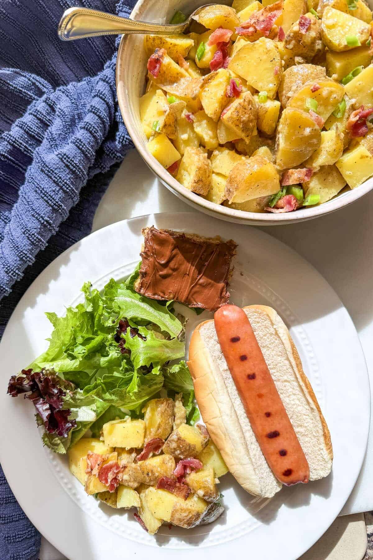 Side dish of no mayo potato salad served alongside grilled hot dog and summer cookout foods.
