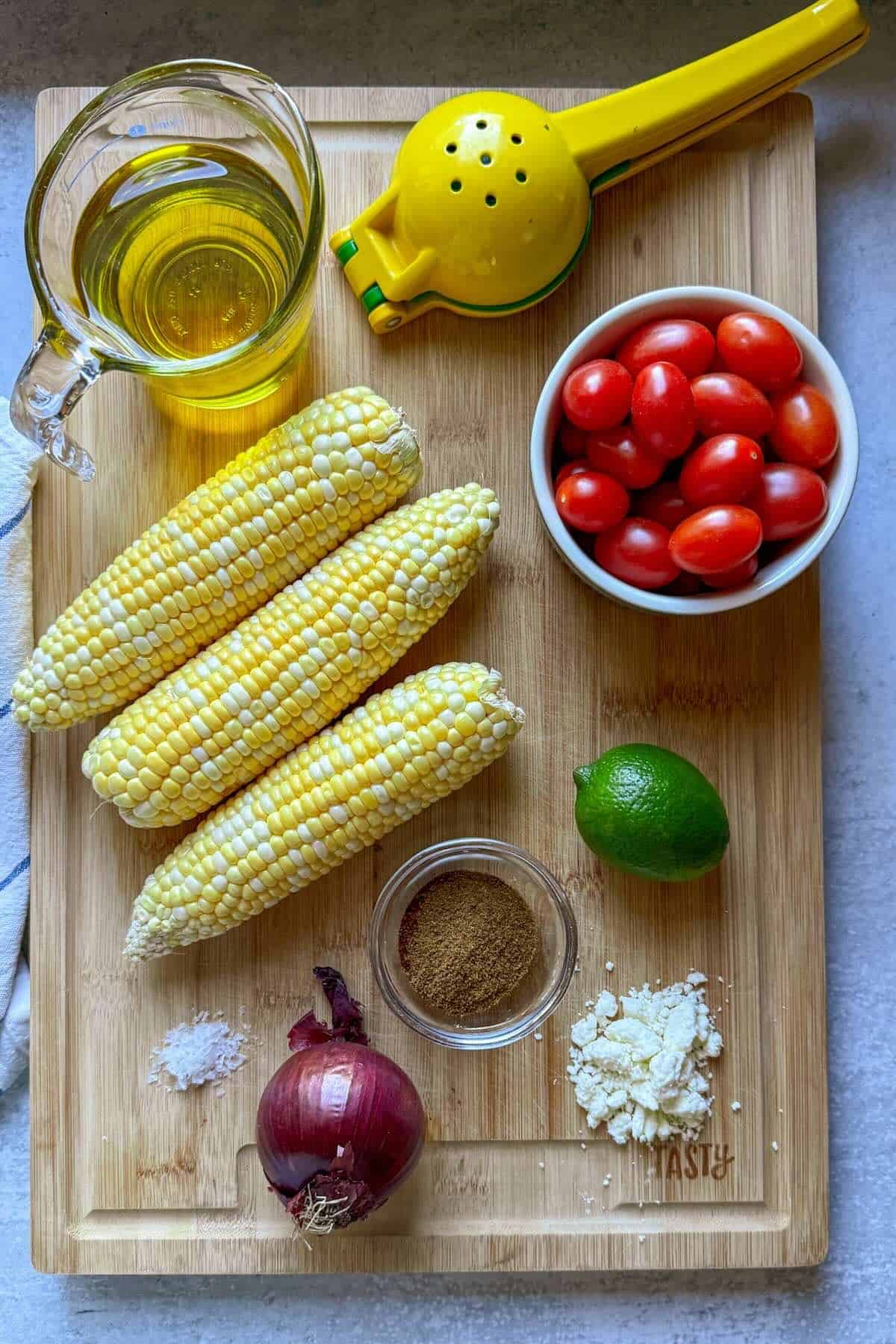 Ingredients to make a corn salad for summer with sweet corn, tomatoes, feta and a chili lime dressing.