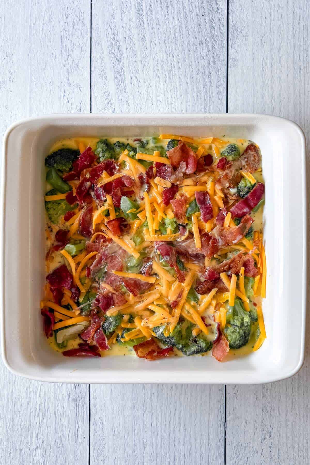 Unbaked bacon broccoli breakfast casserole in an 8x8 baking dish before going into the oven.