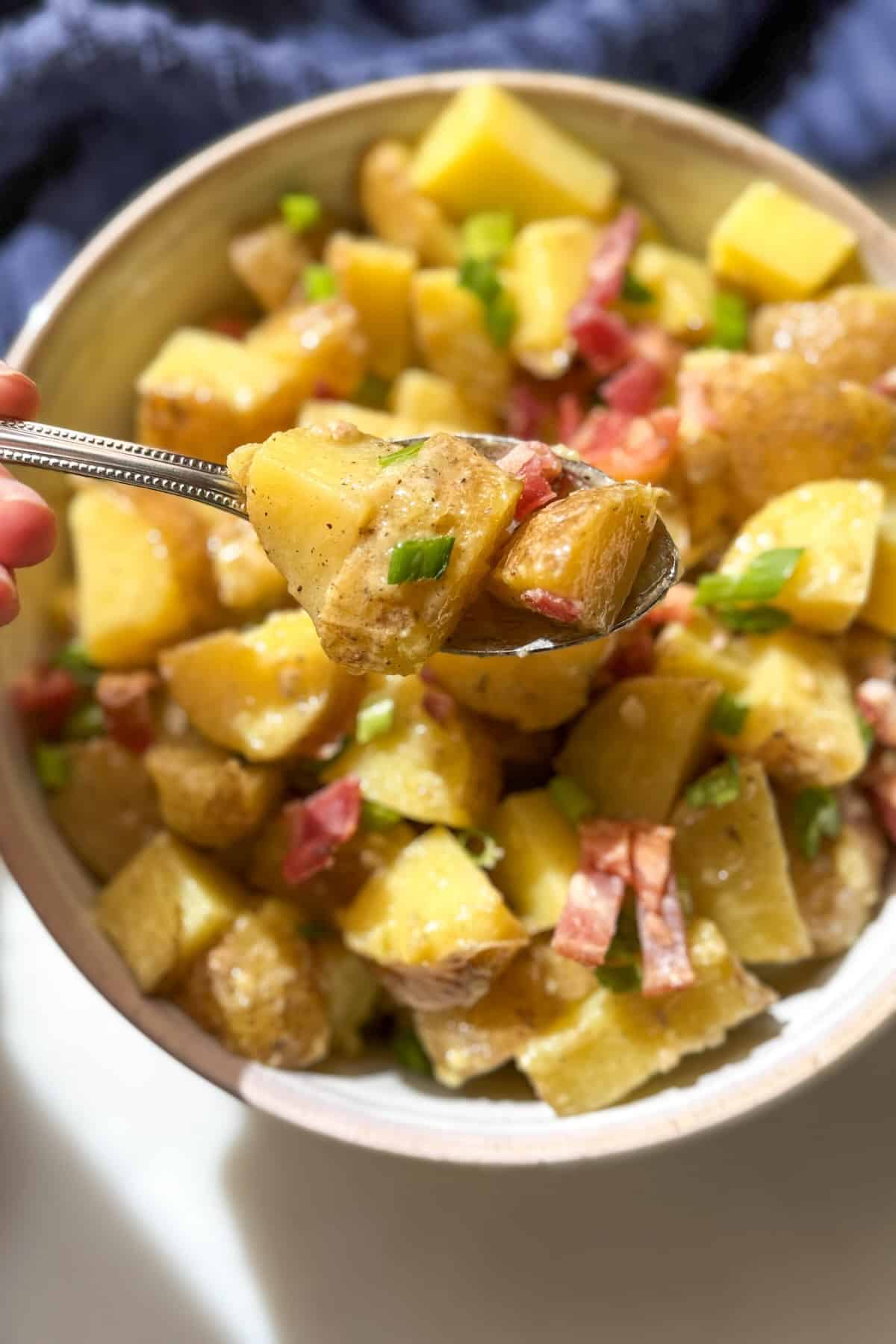 Spoonful of creamy bacon potato salad without mayonnaise showing the texture of the potatoes and dressing.