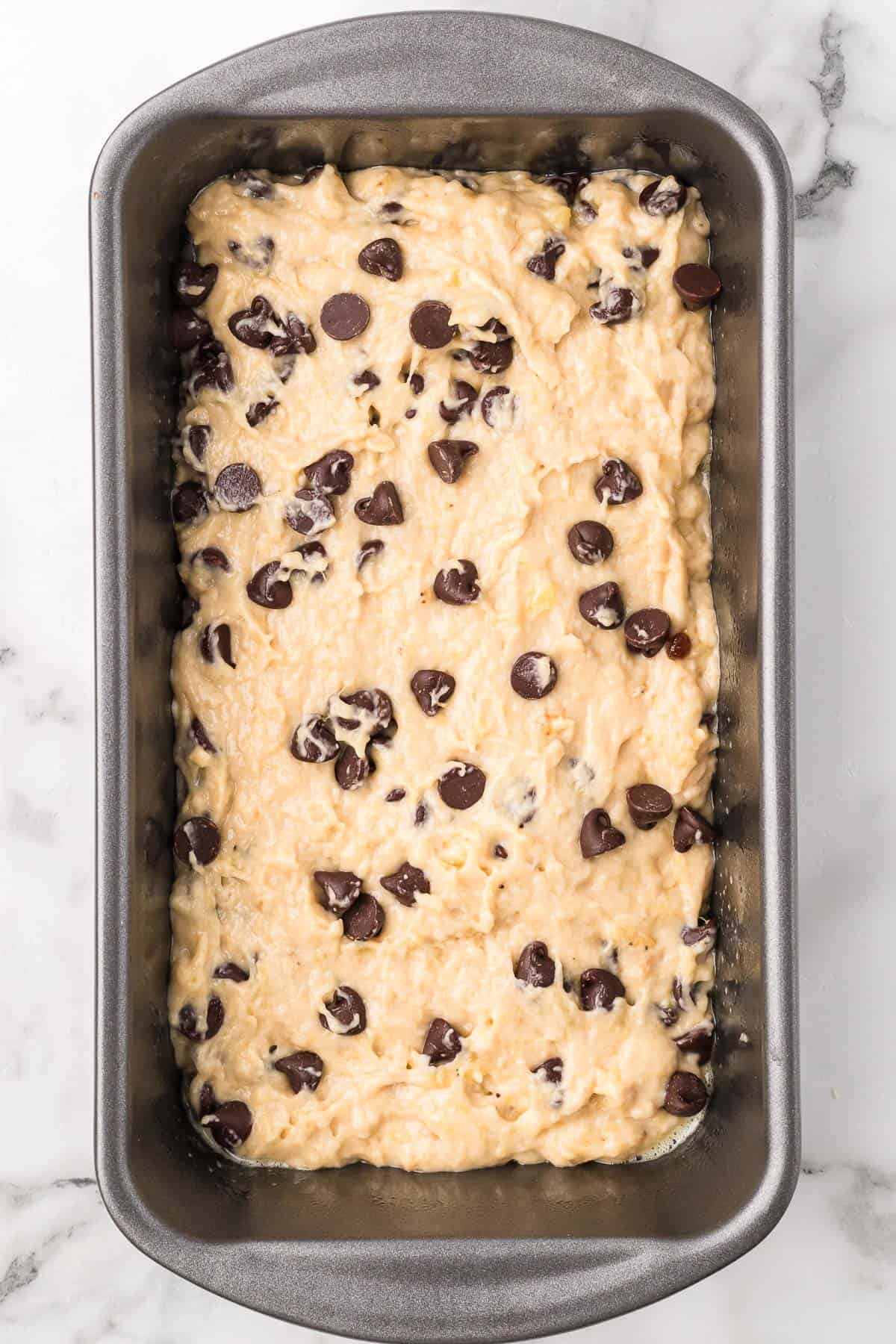 Chocolate chip banana bread batter spread into a prepared loaf pan before baking.