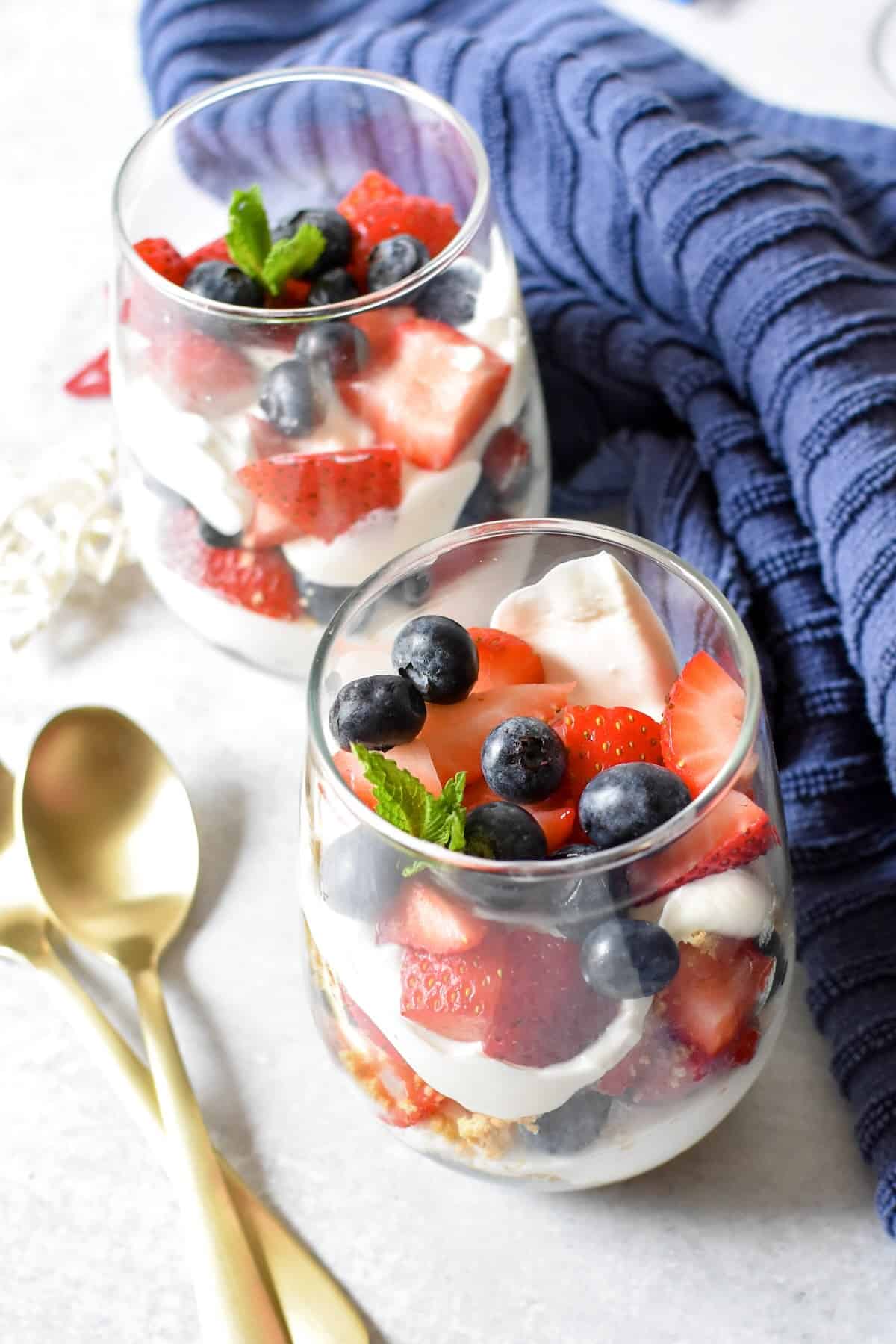 Layers of graham cracker crumbs, cheesecake filling, strawberries, and blueberries in a berry cheesecake parfait.