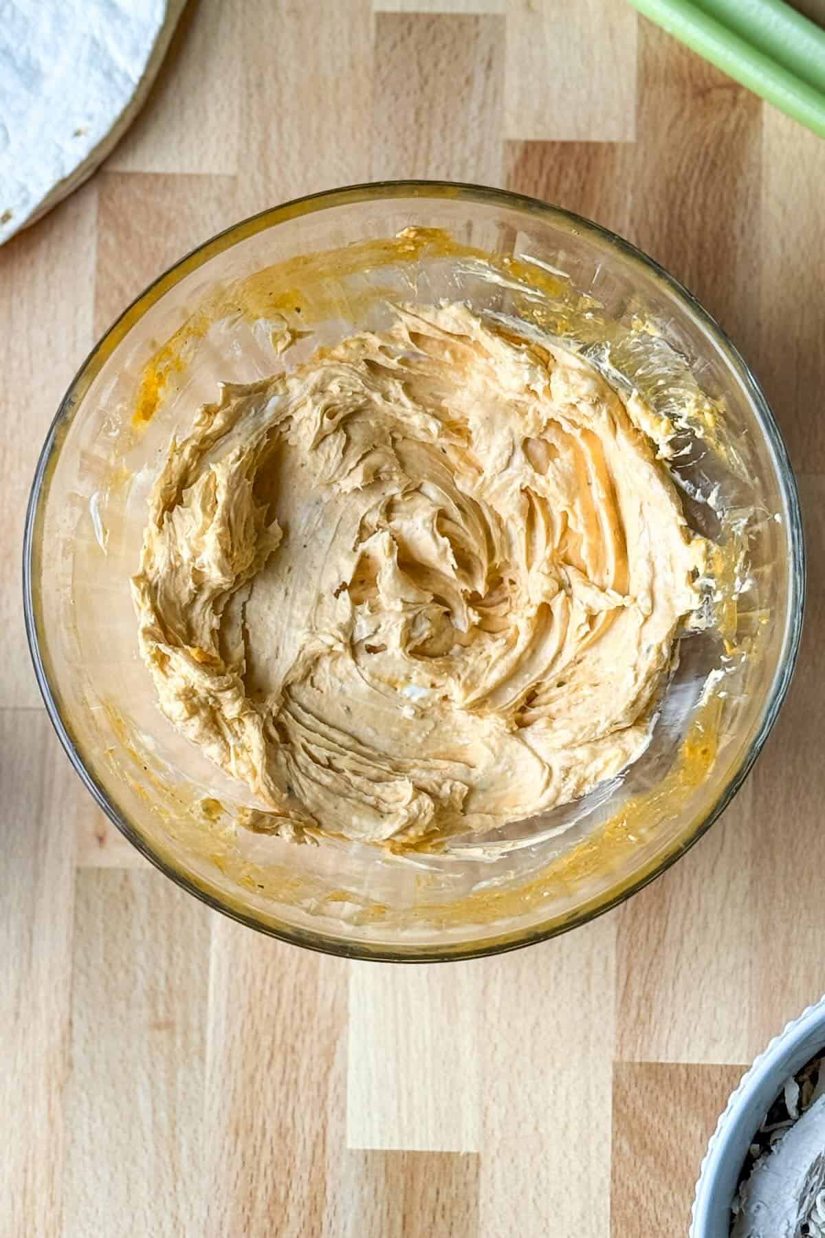Cream cheese, buffalo sauce and shredded cheese mixed in a bowl.