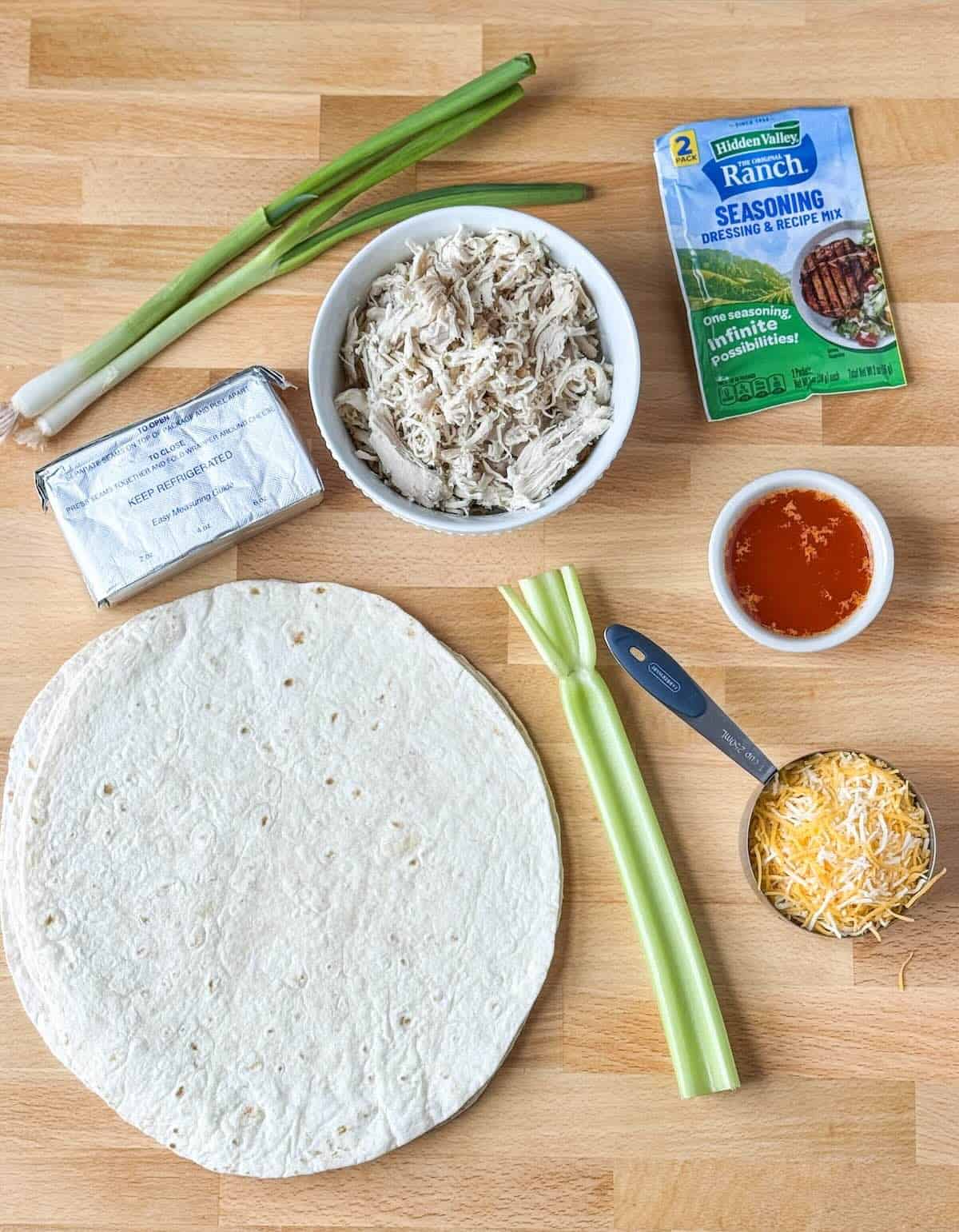 Ingredients needed to make buffalo chicken ranch pinwheels including chicken, cream cheese, ranch dressing, buffalo sauce, celery, and tortillas.