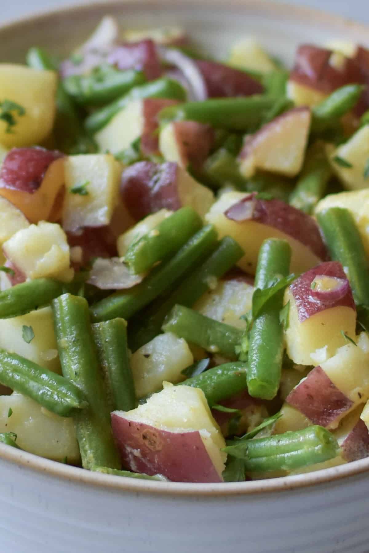 A close up shot of a bowl of cooked red potatoes and cut green beans topped with a vinegar dressing.