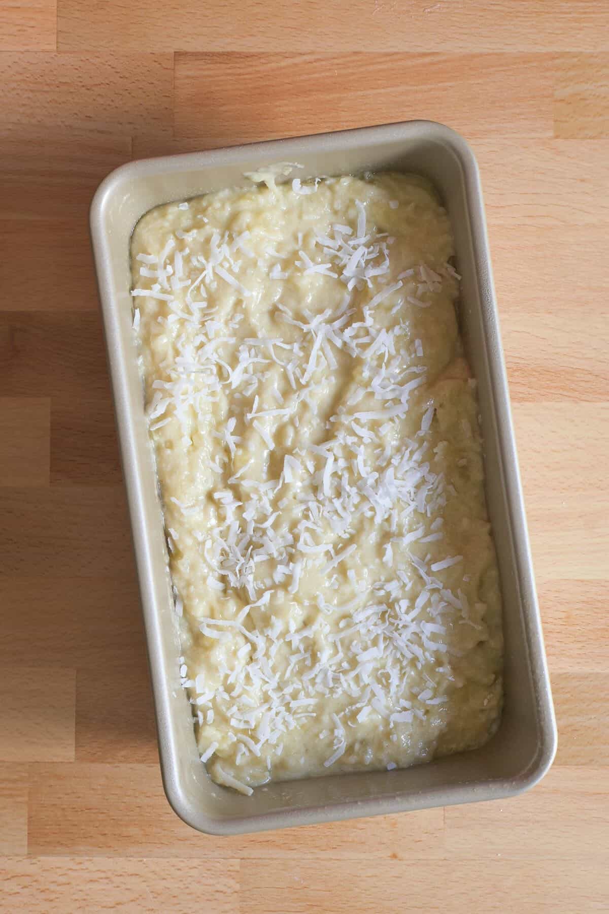 Hawaiian banana bread batter in a loaf pan before baking, sprinkled with shredded coconut.