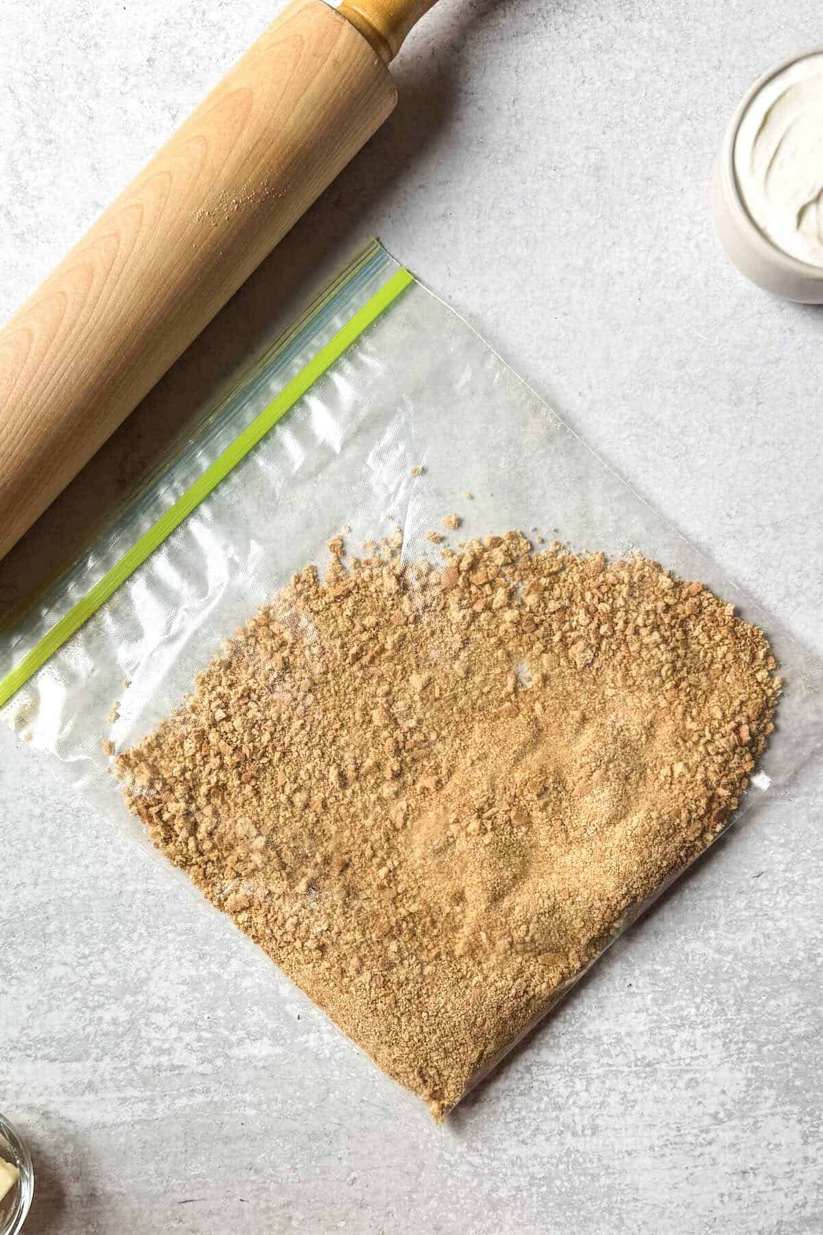 Crushed graham crackers in a zip top bag with a rolling pin to make graham cracker crumbs.