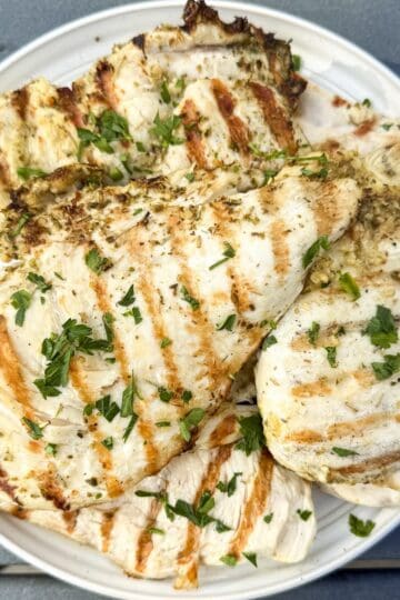 Easy herb grilled chicken sliced and served on a platter with a light parsley garnish.