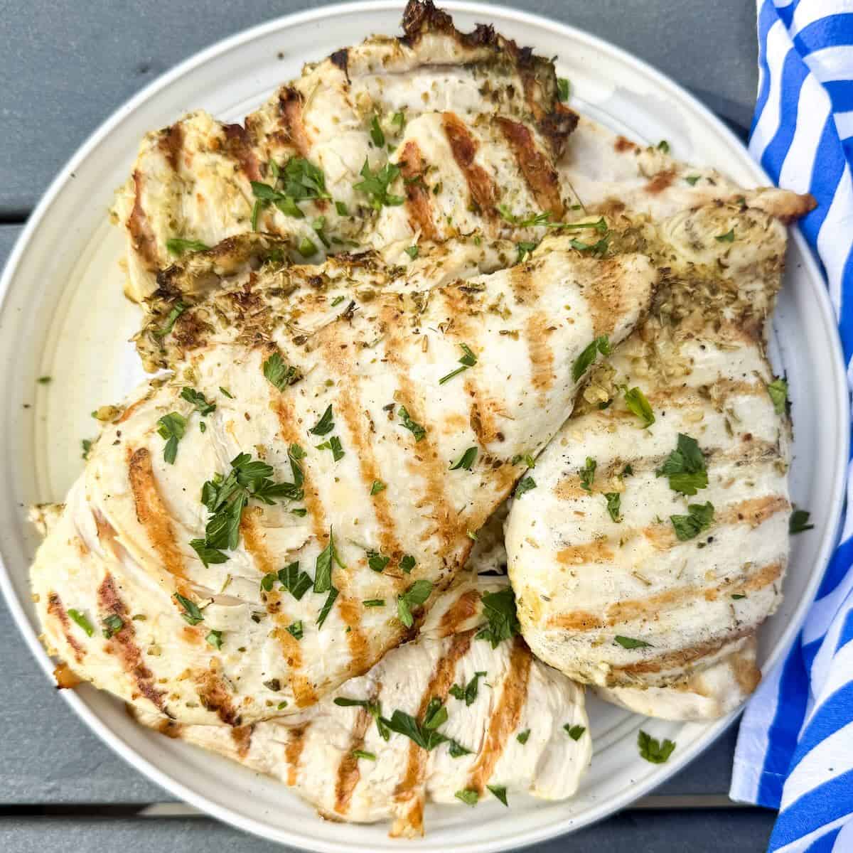 Easy herb grilled chicken sliced and served on a platter with a light parsley garnish.