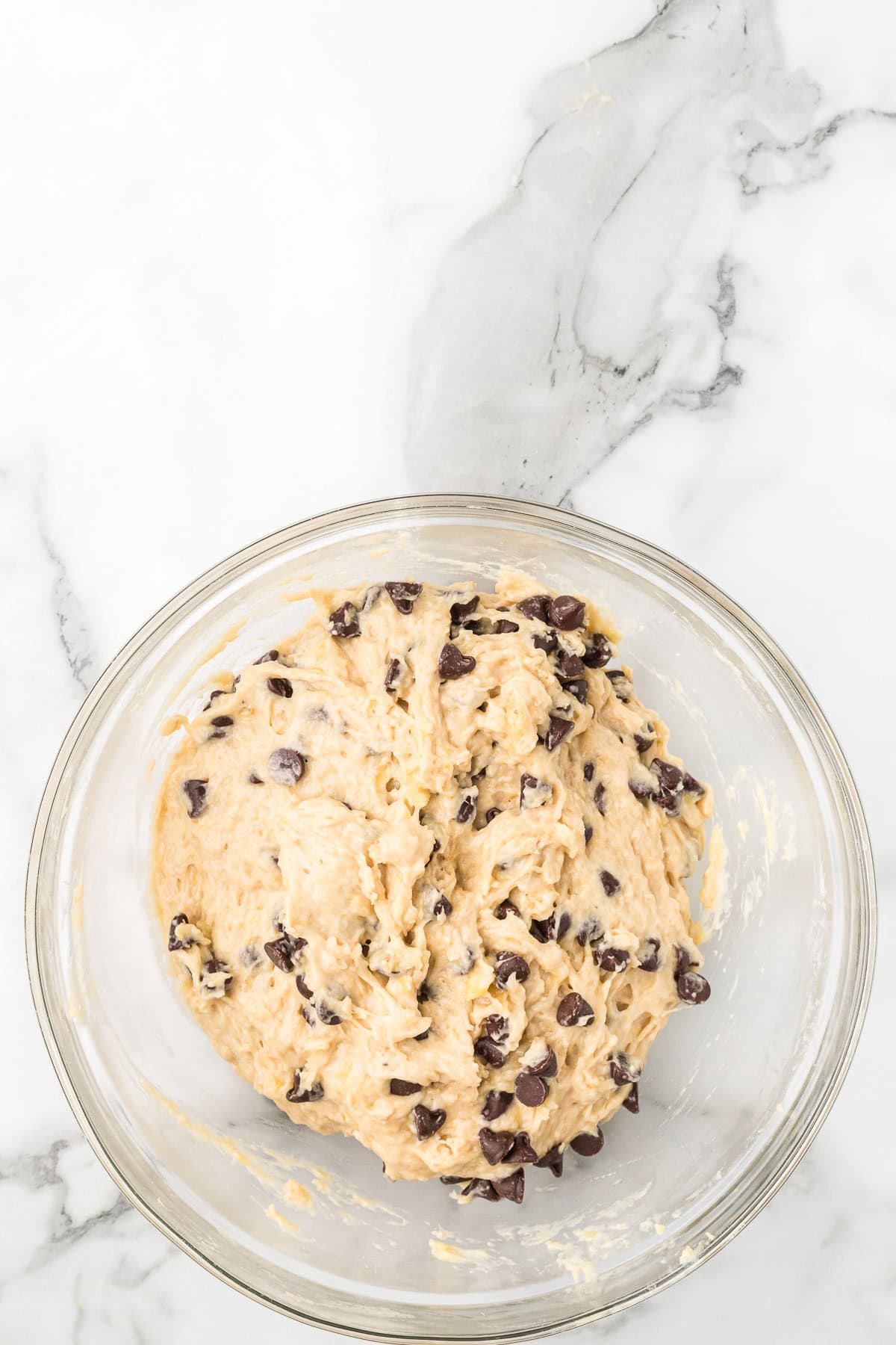 Chocolate chips being folded into banana bread batter before baking.
