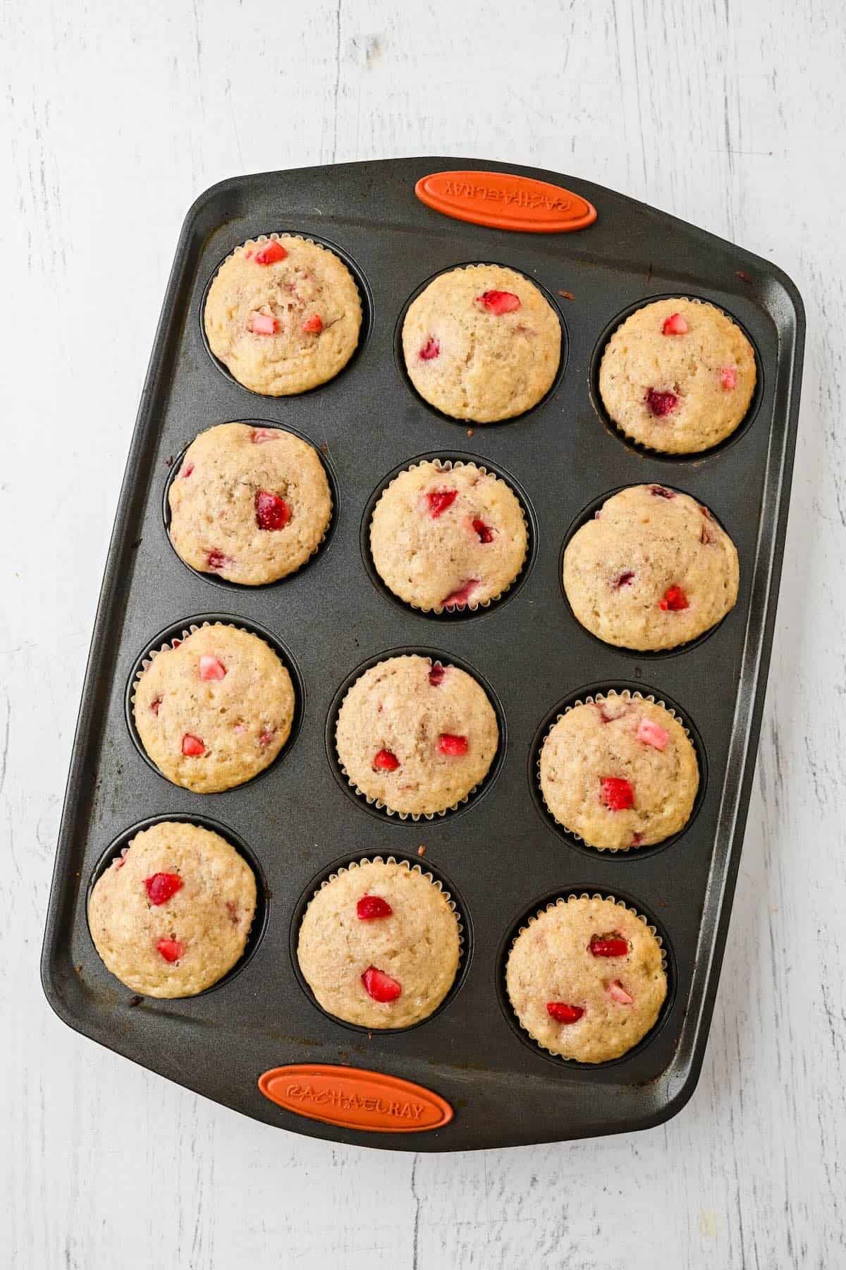 Freshly baked strawberry banana muffins cooling in a muffin pan.
