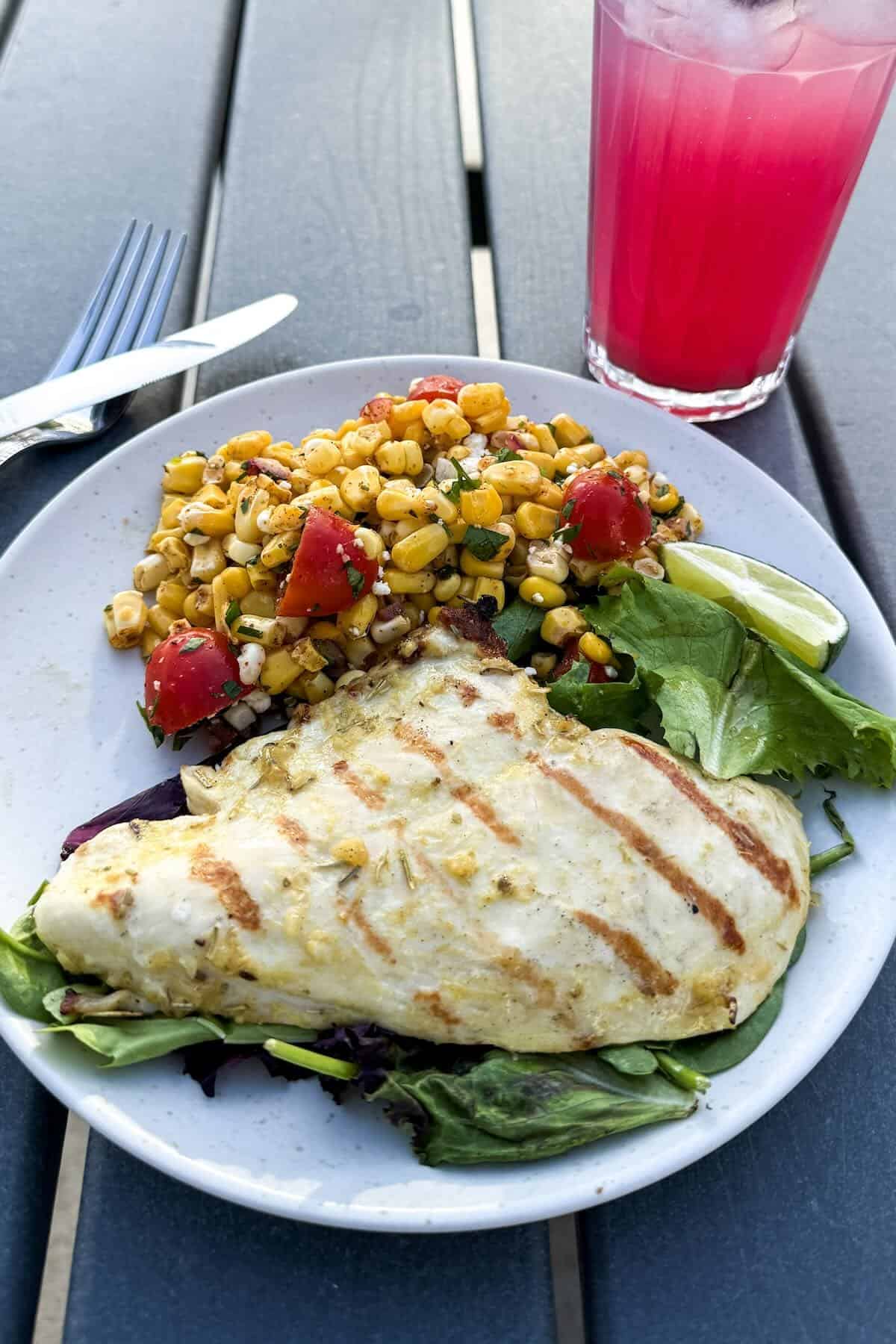 Herb grilled chicken breast served with corn salad and a refreshing summer drink.