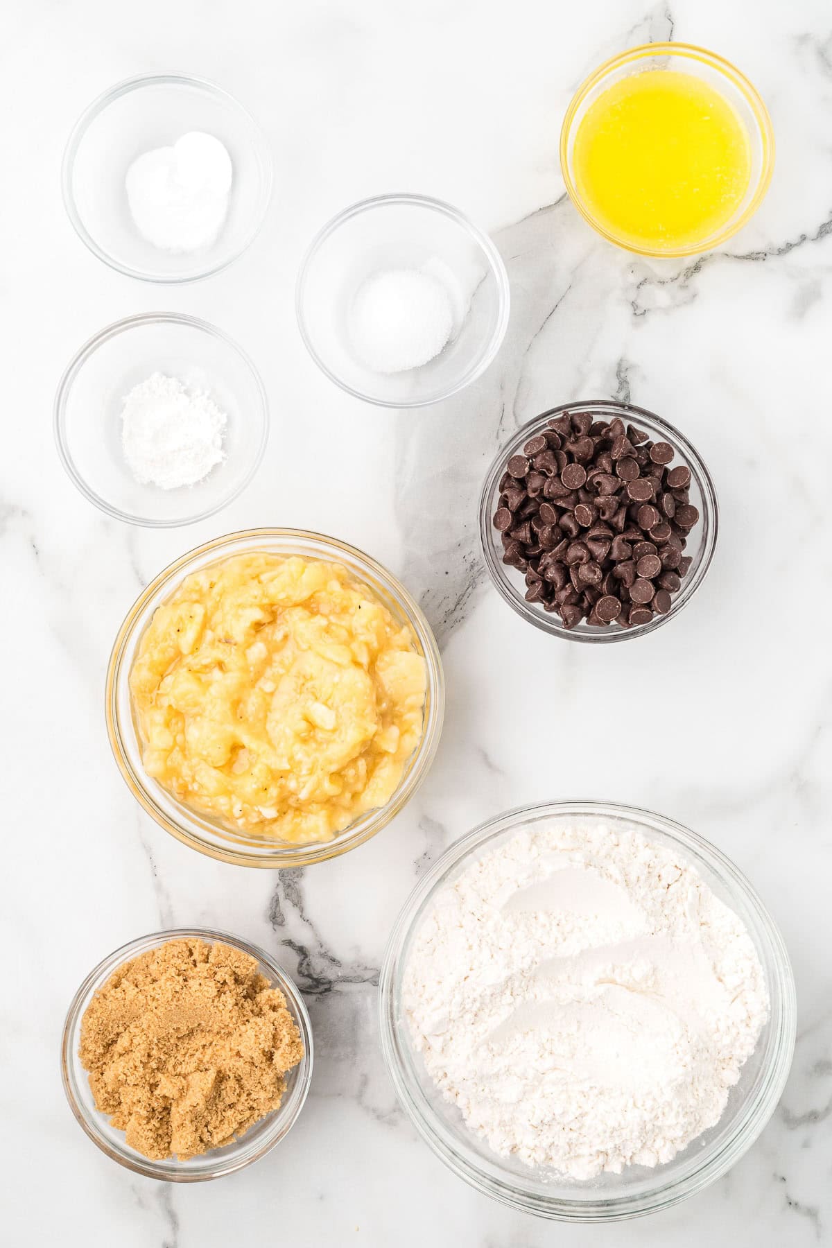 Ingredients for chocolate chip banana bread including ripe bananas, flour, brown sugar, butter, and chocolate chips.