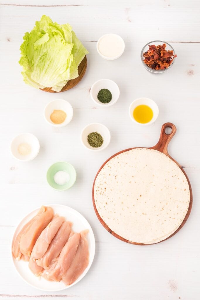 Ingredients for chicken bacon ranch wraps including chicken, bacon, tortillas, lettuce, ranch dressing, and seasonings.