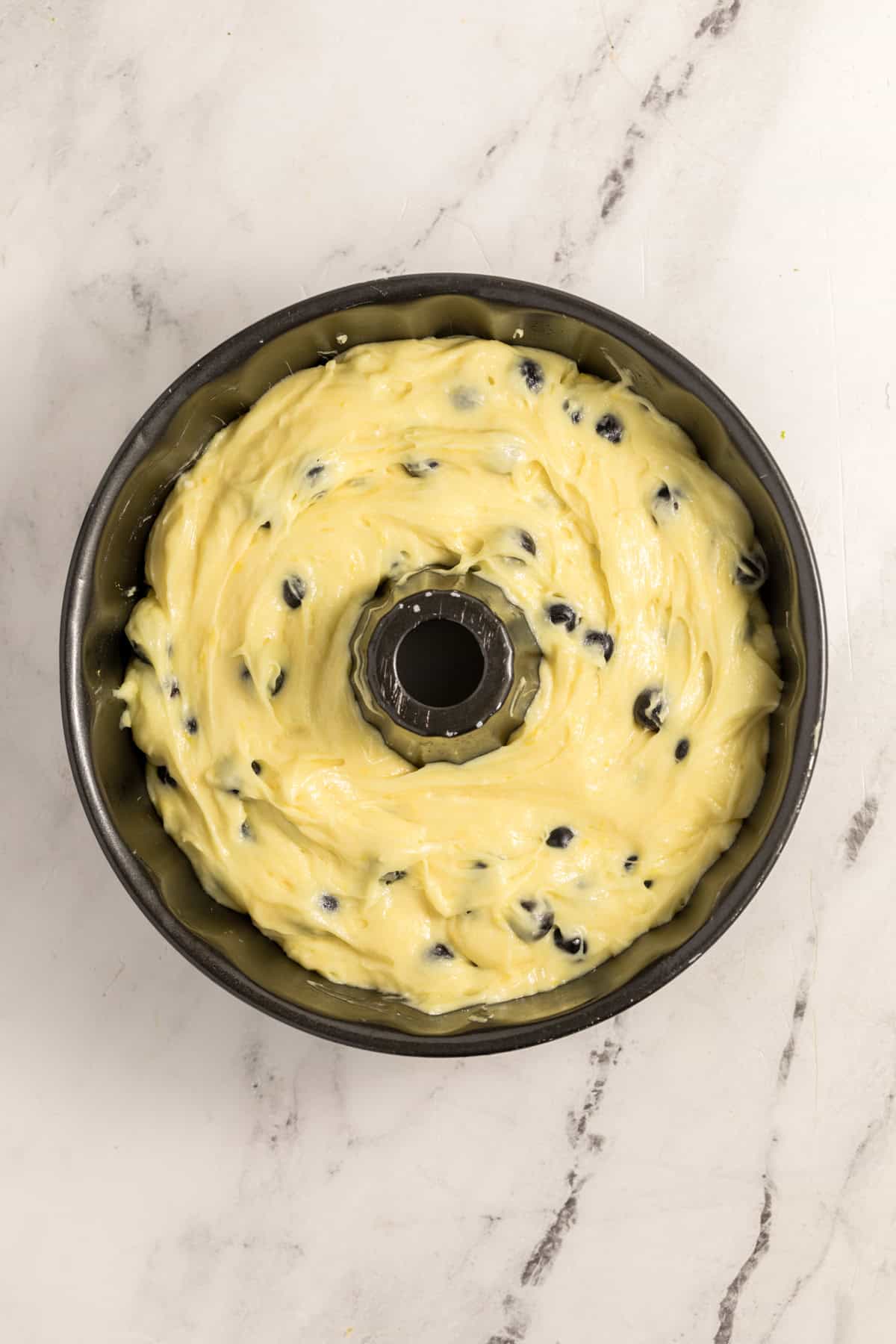 Lemon blueberry cake batter spread in a greased bundt pan before baking.
