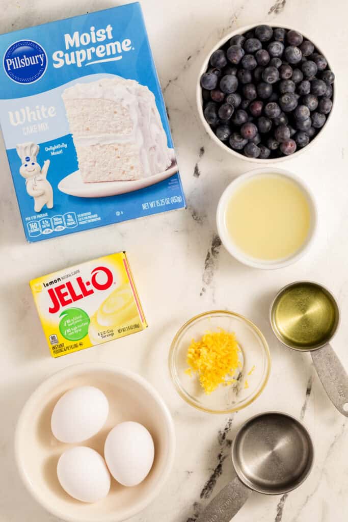 Ingredients for lemon blueberry bundt cake including cake mix, lemon pudding, blueberries, lemons, oil, and egg whites.