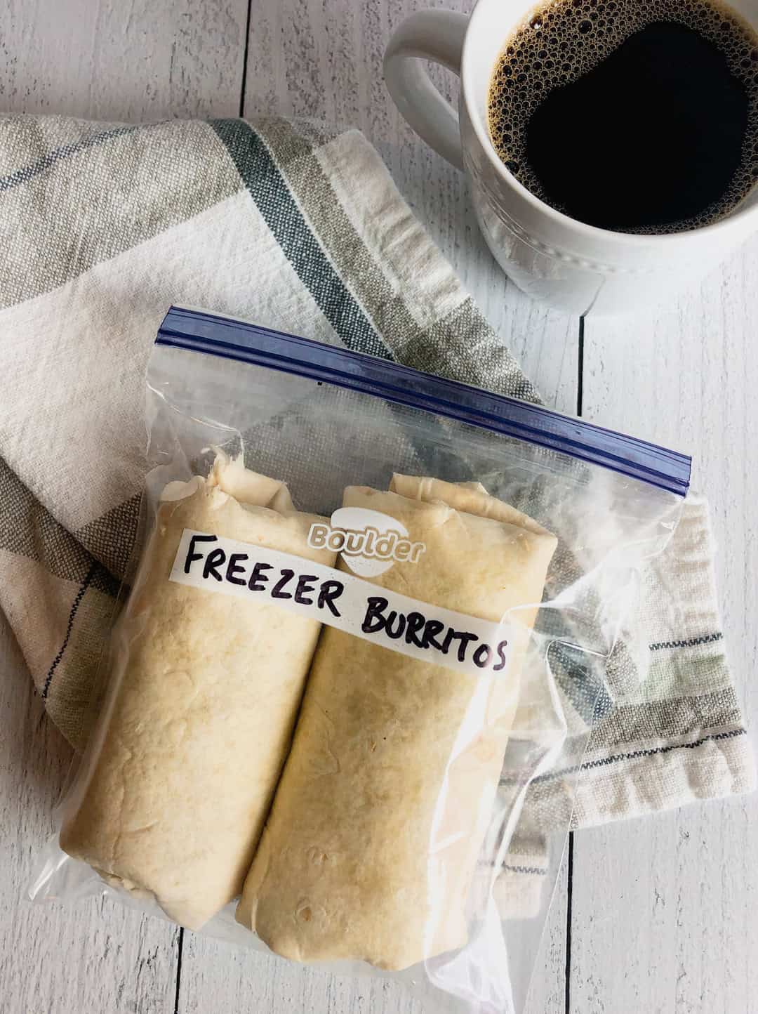 A bag labeled with breakfast burritos to go in the freezer alongside a cup of coffee.