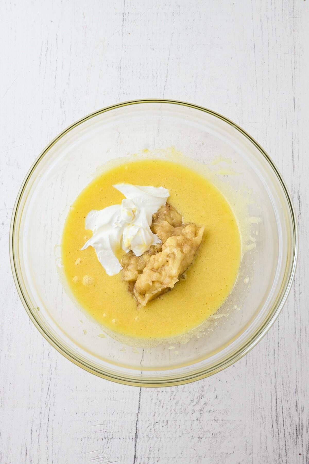 Mashed ripe bananas and sour cream in a mixing bowl for strawberry banana muffin batter.