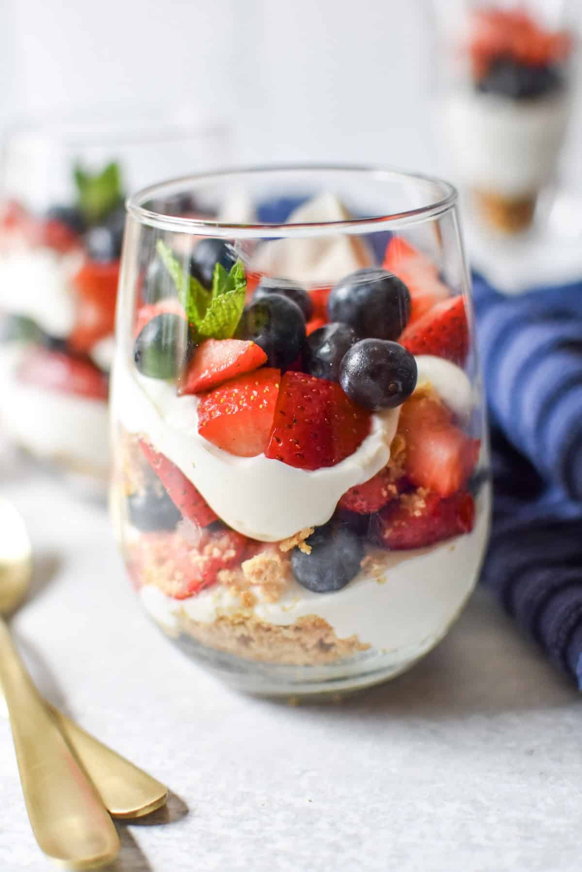 No bake cheesecake parfaits layered with graham cracker crumbs, cheesecake filling, strawberries, and blueberries in parfait glasses.