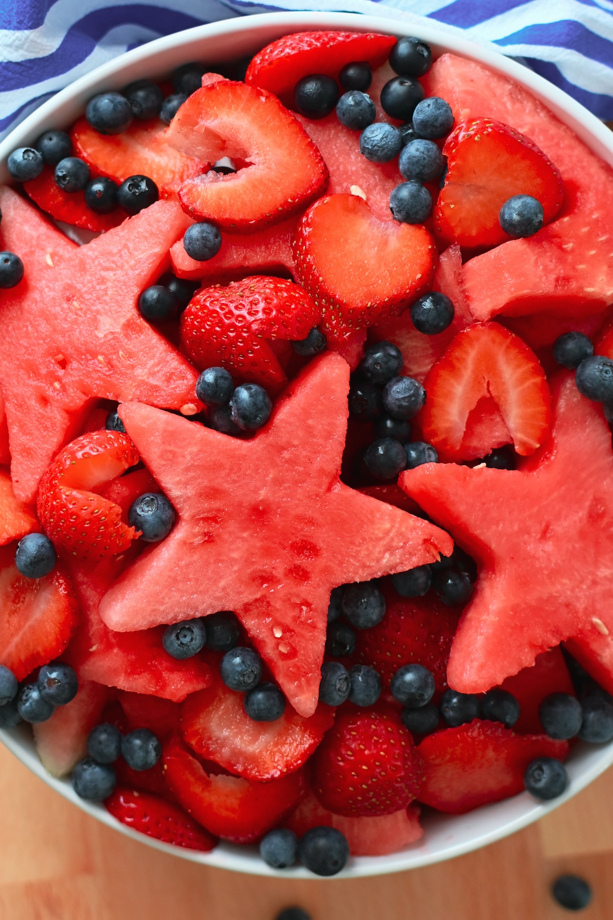 Overhead view of red white and blue fruit salad in a white serving bowl.