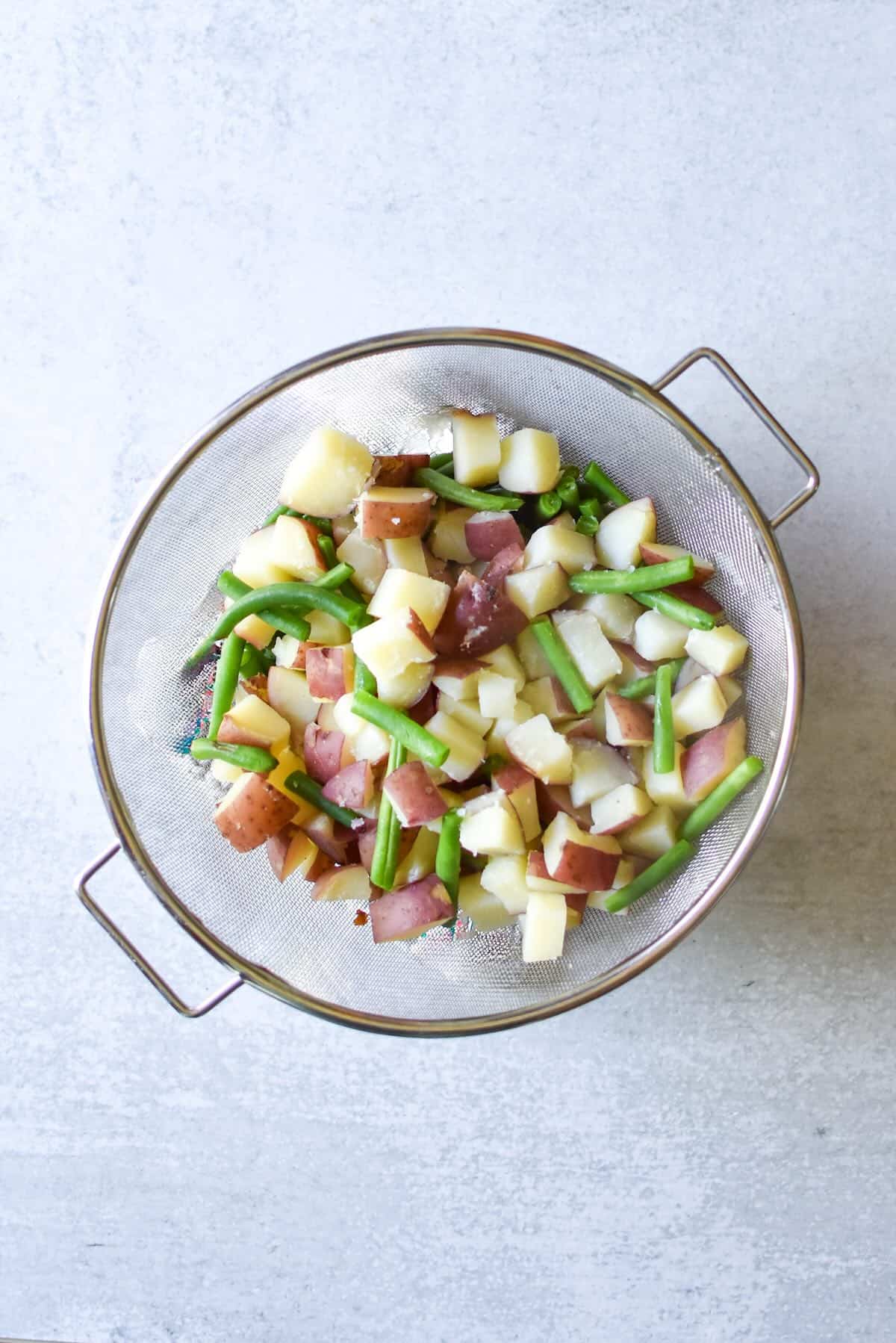 Chopped red potatoes and trimmed green beans in a strainer basket after cooking. 
