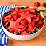 Red white and blue fruit salad with watermelon stars, sliced strawberries, and blueberries in a white bowl.