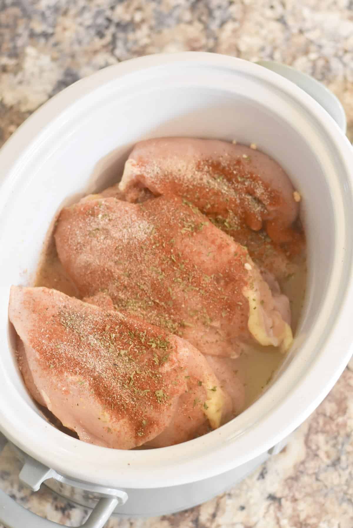 Seasoned chicken breasts in a slow cooker before cooking.