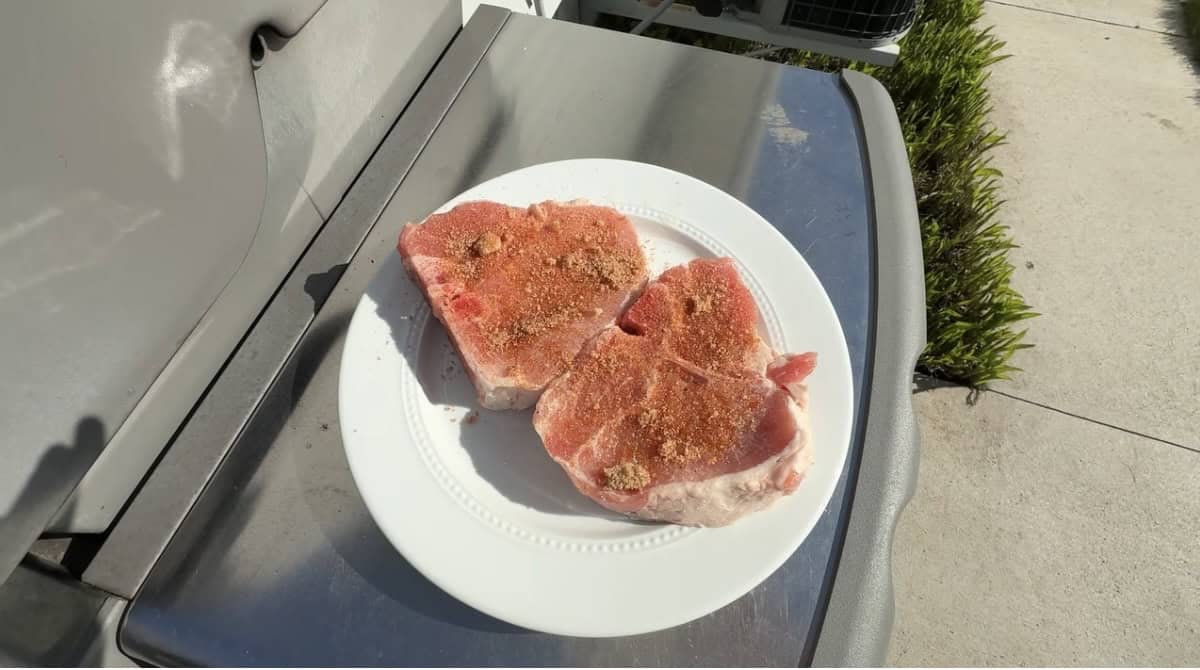 Applying farmhouse BBQ rub to bone-in pork chops before grilling.