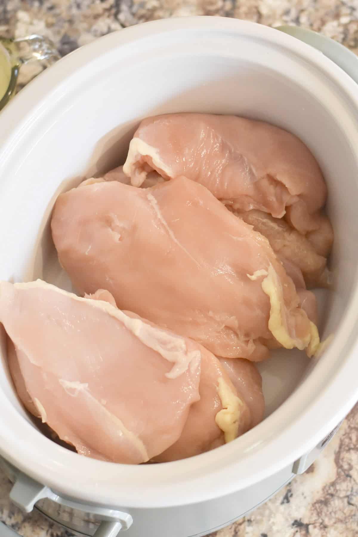 Raw chicken breasts in a slow cooker.