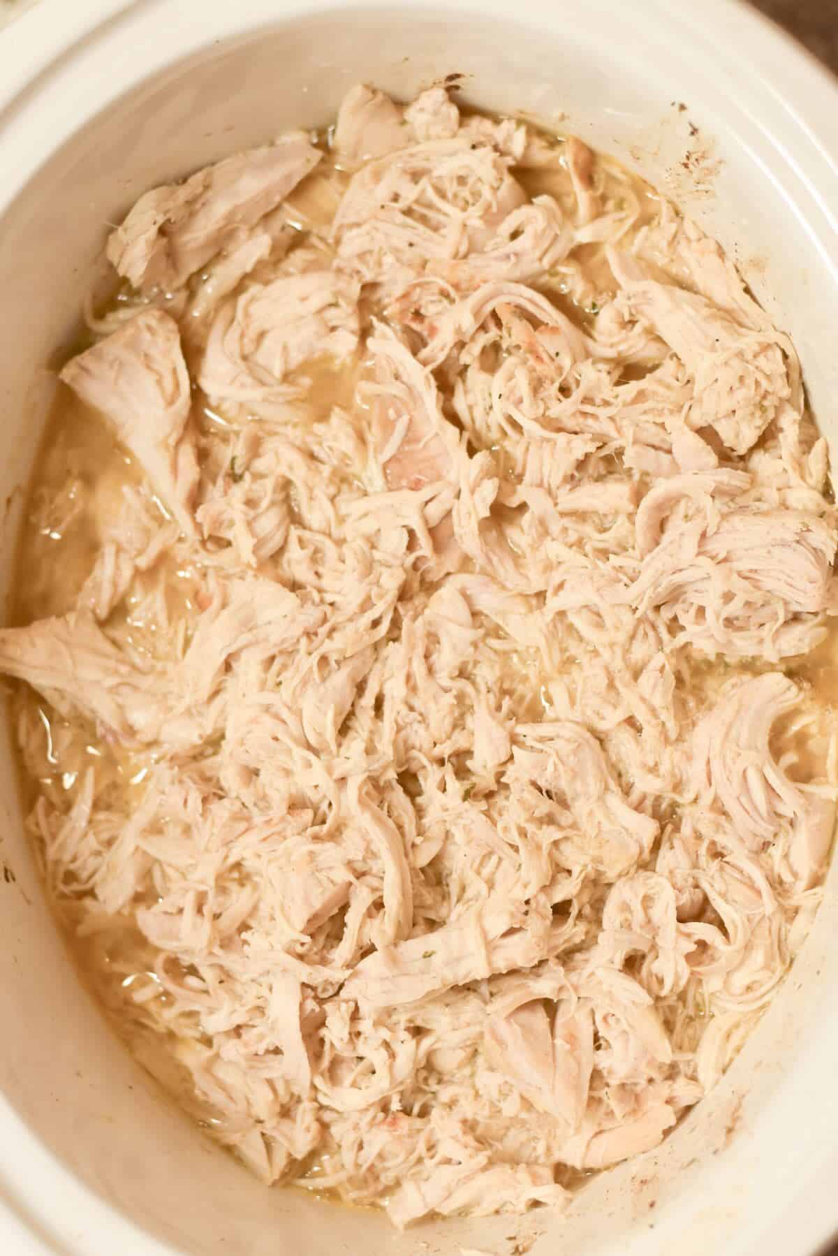Shredded chicken mixed with cooking juices in a slow cooker.