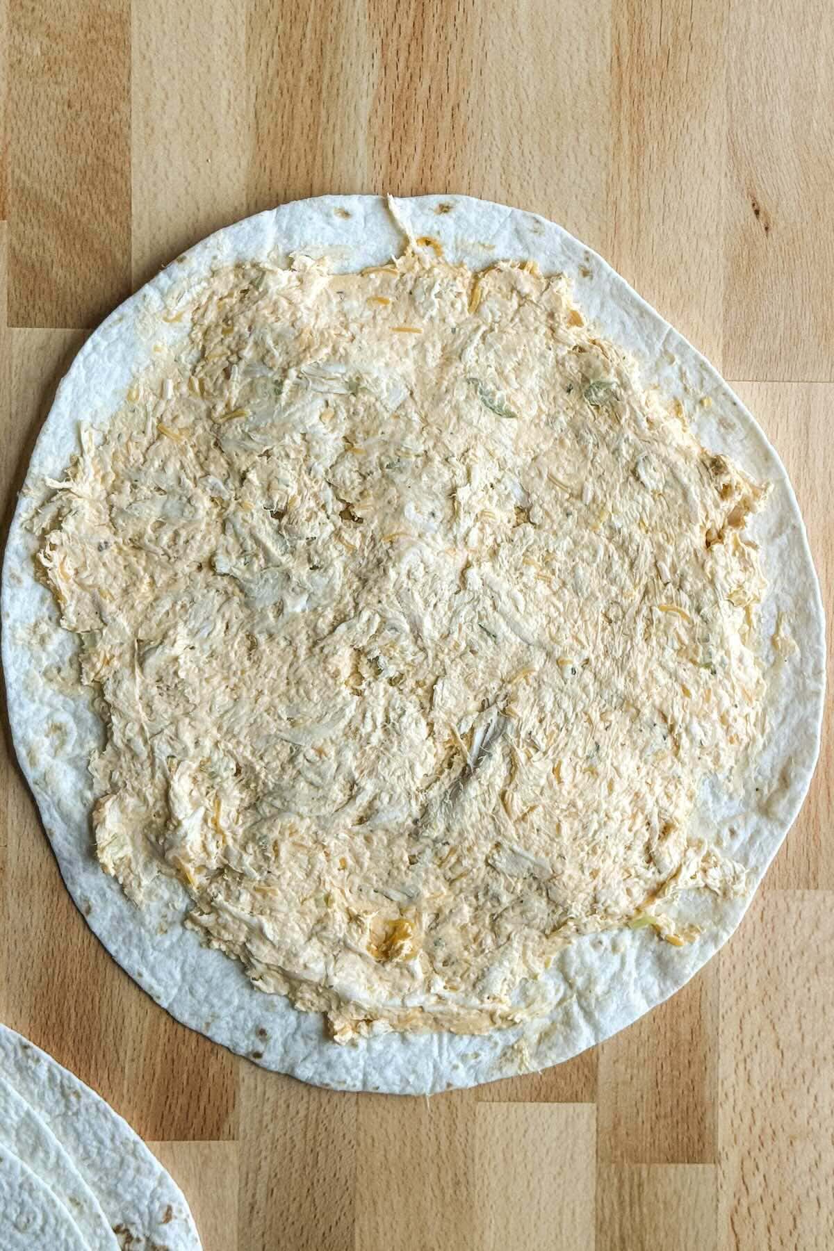 Spreading buffalo chicken filling over a flour tortilla before rolling.