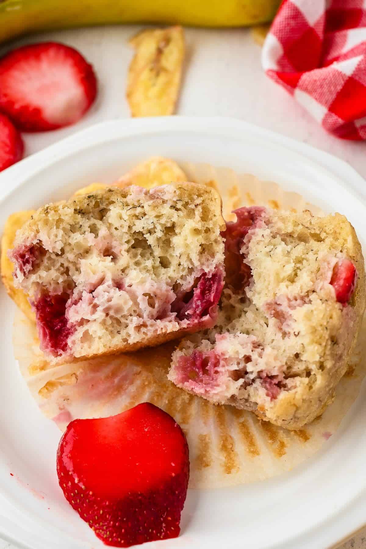 Strawberry banana muffin split in half showing the soft interior and fresh strawberries.