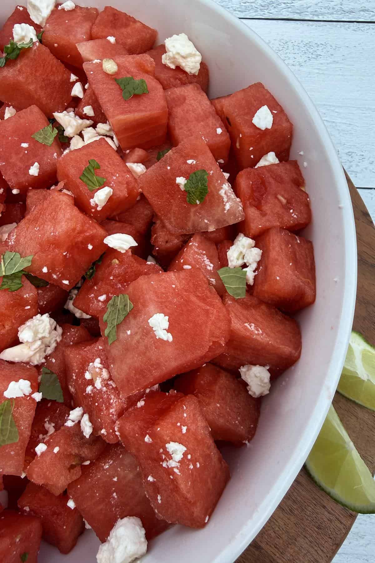 Watermelon feta mint salad served in a white bowl with lime wedges.