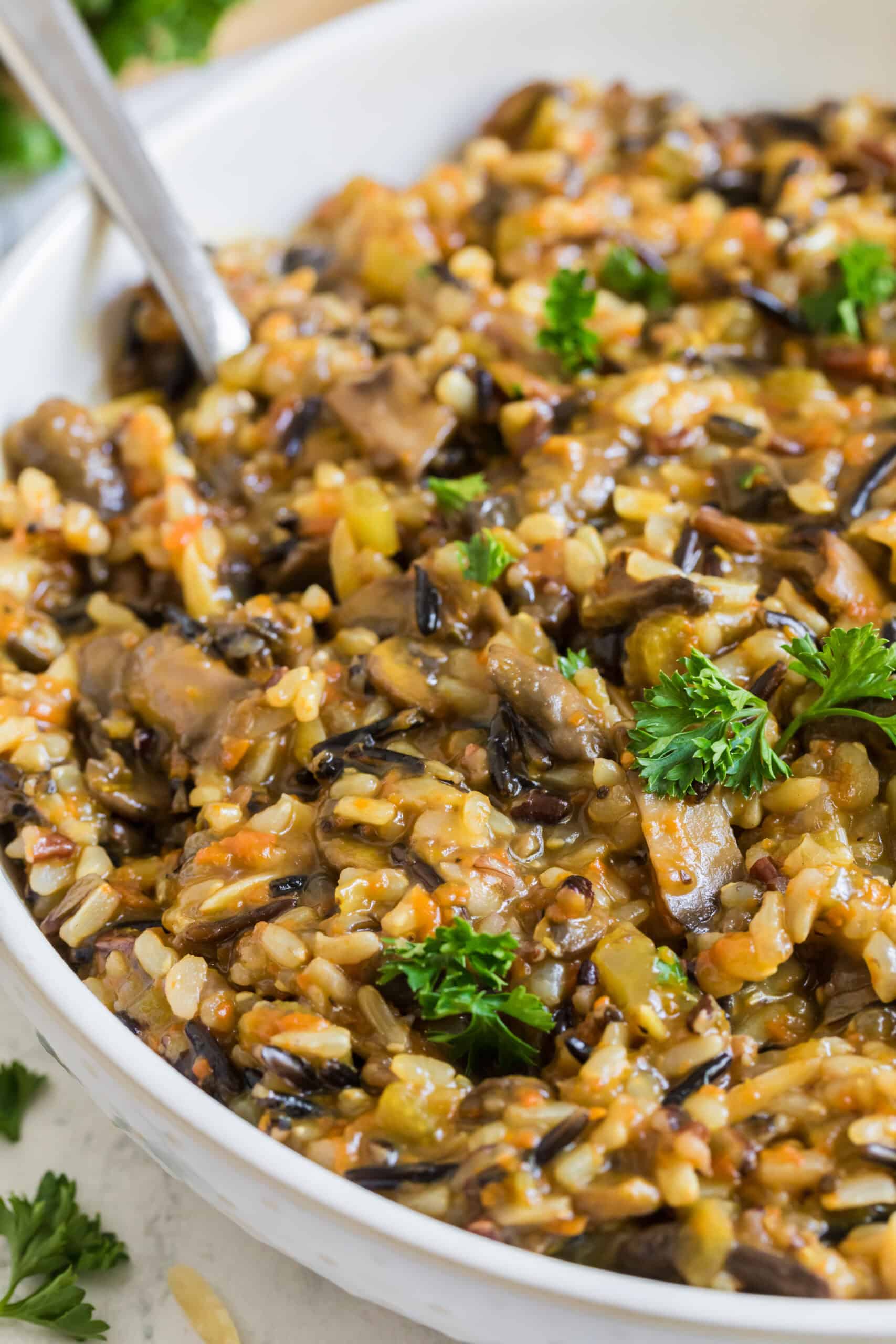 Instant Pot wild rice pilaf with mushrooms, carrots, celery, herbs, and toasted almonds in a white serving bowl.