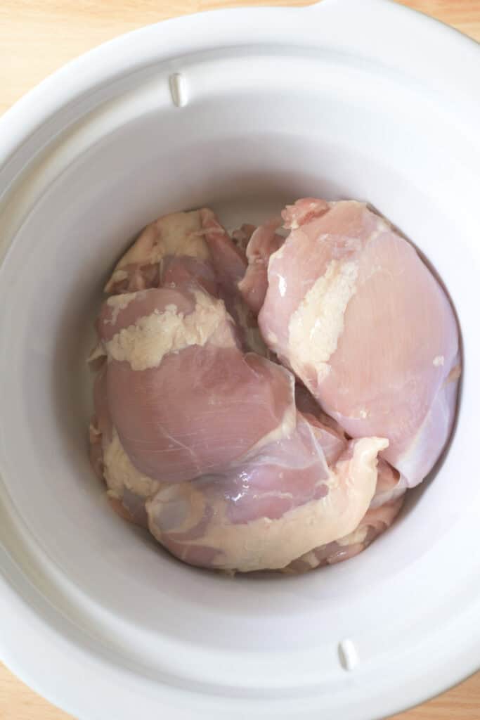 Boneless skinless chicken thighs placed in a slow cooker before adding the remaining ingredients.