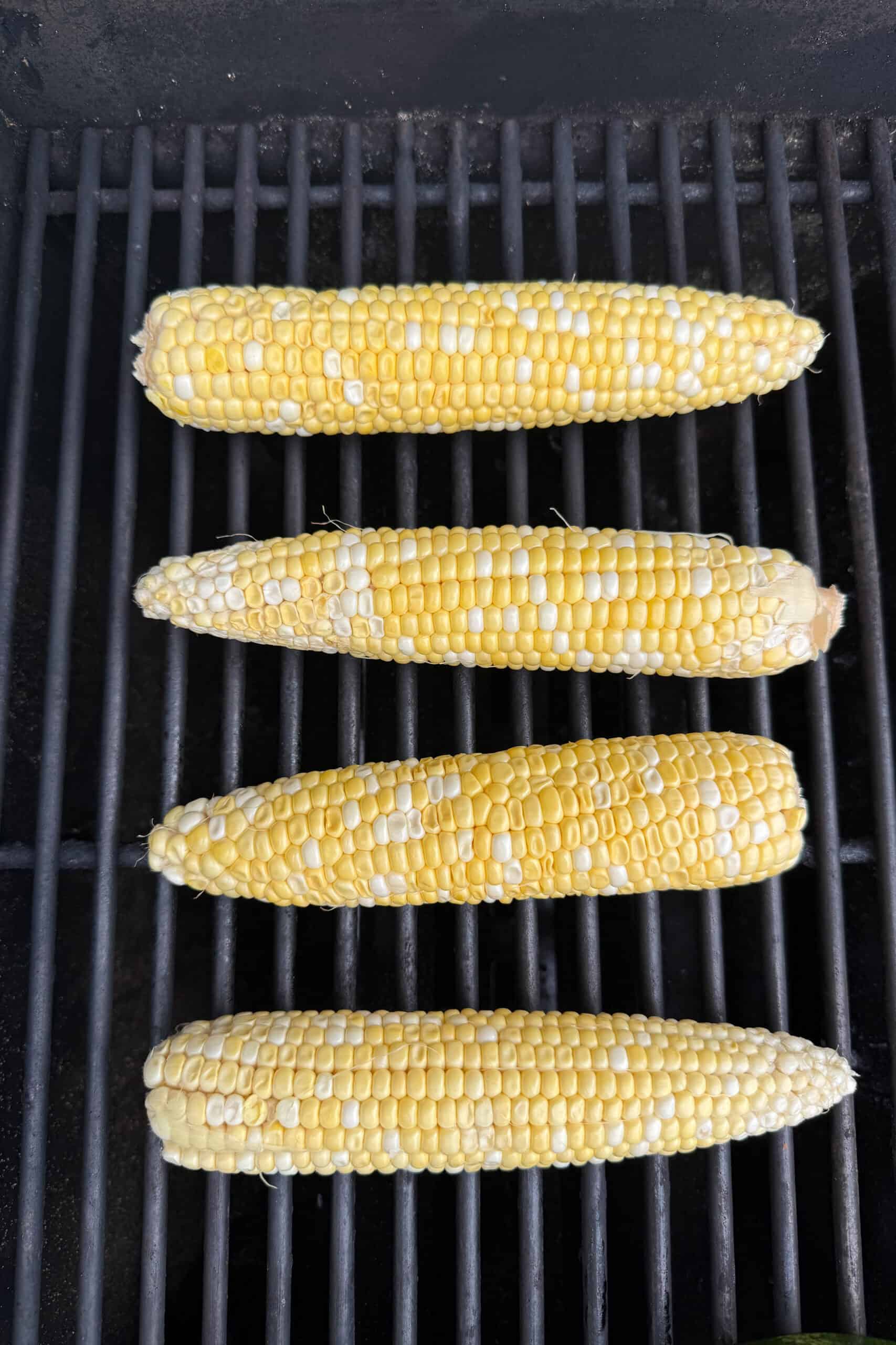 Fresh sweet corn cooking directly on grill grates.