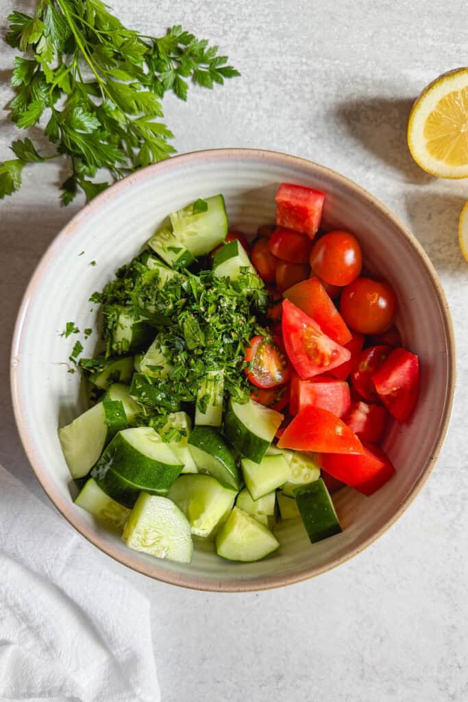 Chopped cucumbers, tomatoes, and parsley in a mixing bowl before adding the dressing