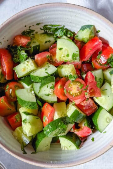 Bowl of cucumber tomato salad with parsley, olive oil, and lemon dressing.