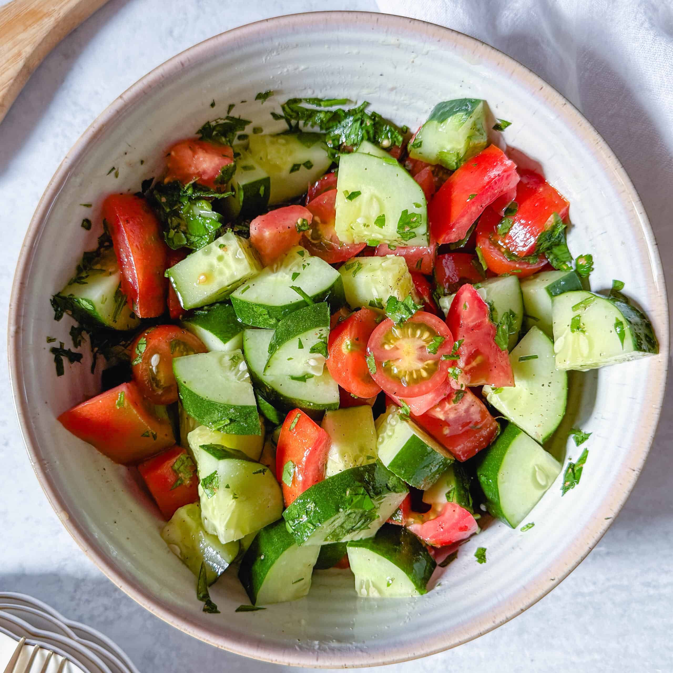 Bowl of cucumber tomato salad with parsley, olive oil, and lemon dressing.