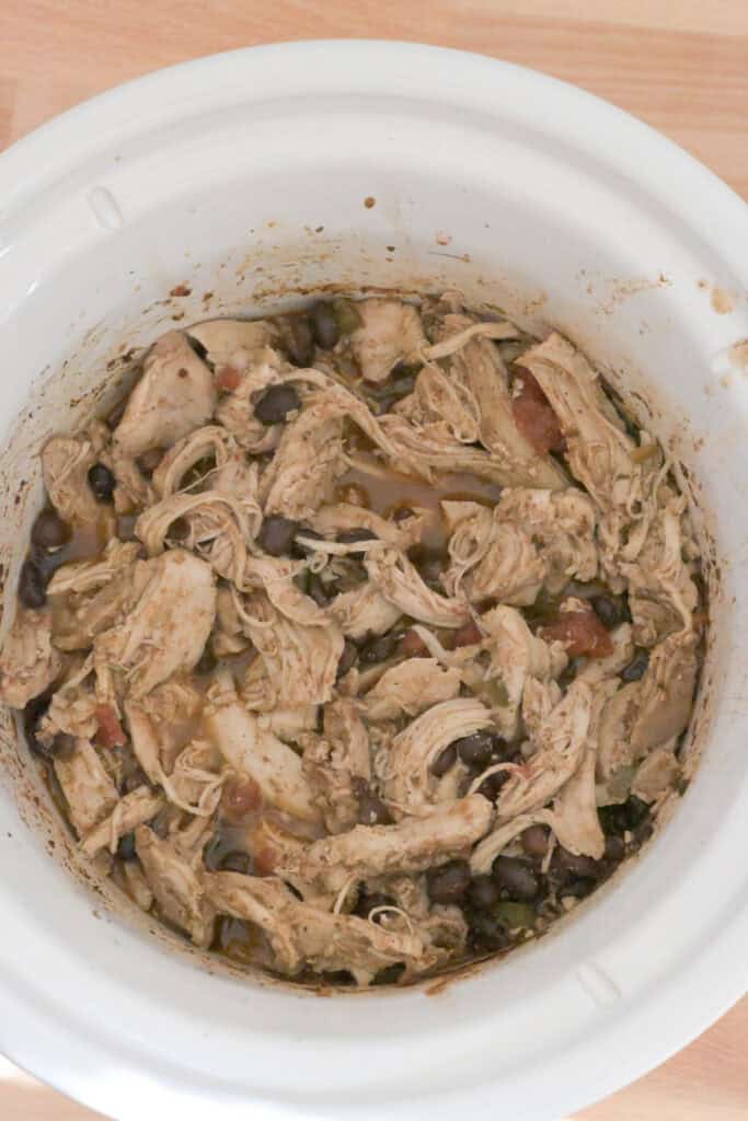 Shredded Mexican chicken mixed with black beans and tomatoes in the slow cooker.