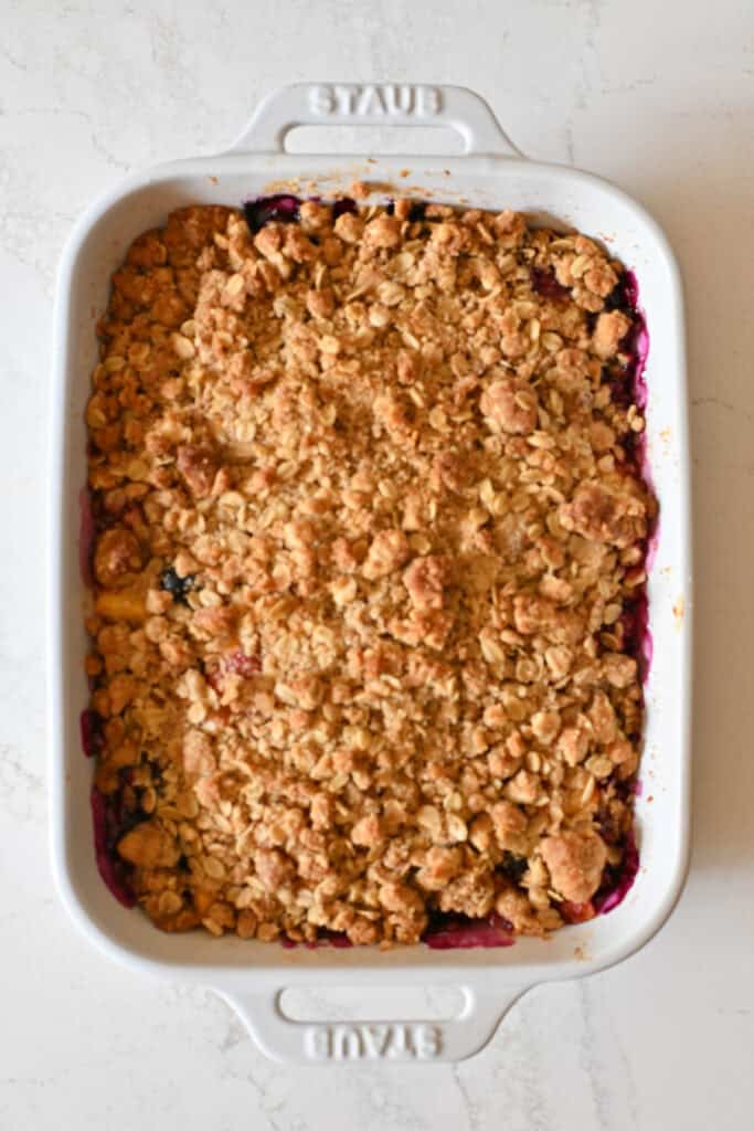 A baked blueberry peach cobbler with bubbly blueberries in a white baking dish.