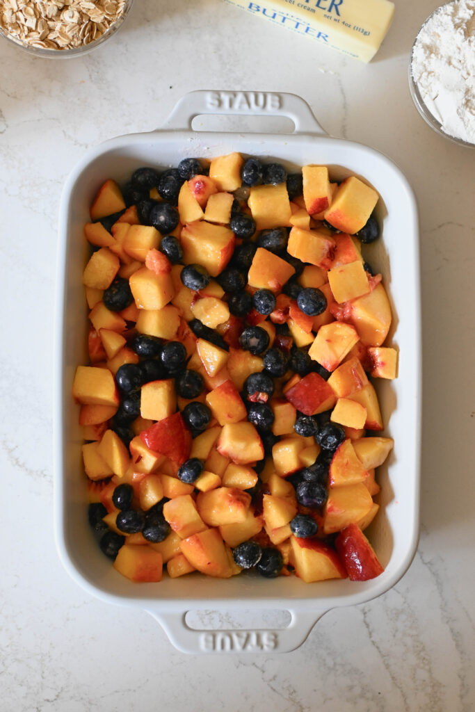 Diced peaches and fresh blueberries mixed in a rectangle baking dish.