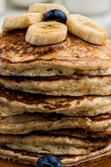 A stack of banana pancakes stopped with maple syrup and banana slices.