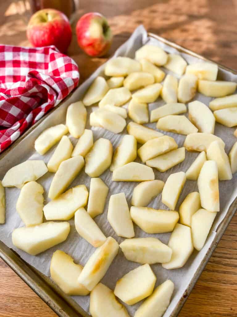 A parchment paper lined sheet pan with apple slices to be frozen.