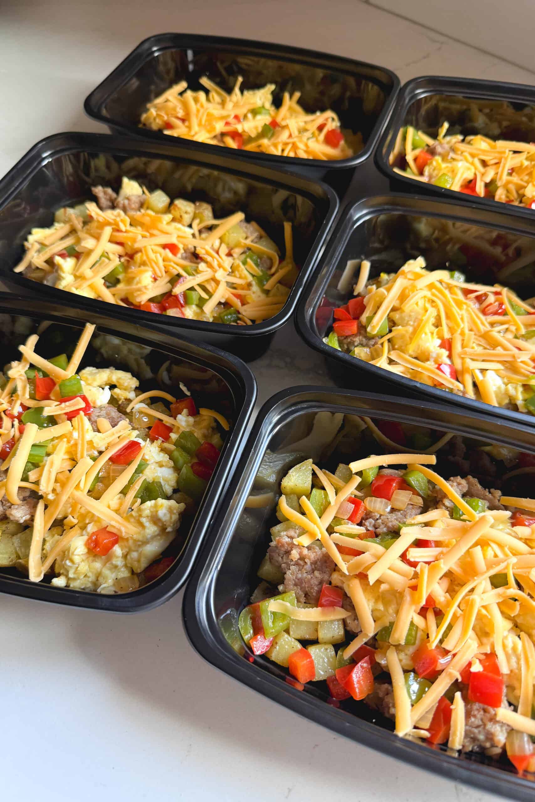 A batch of six breakfast bowls topped with cheese on the counter.