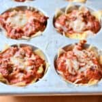 Individual lasagna cups baked in a muffin tin topped with cheese.