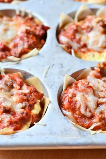Individual lasagna cups baked in a muffin tin topped with cheese.