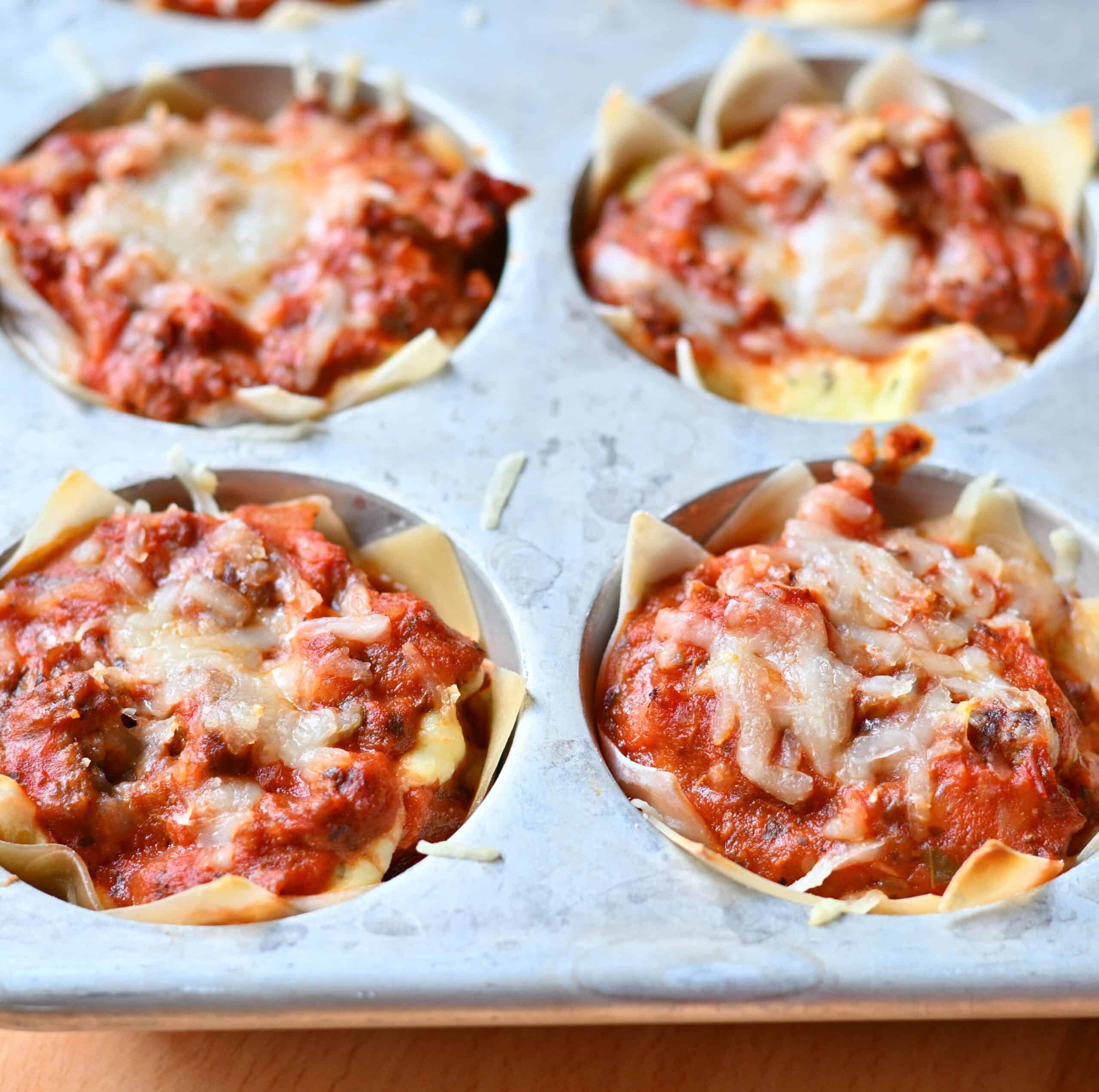 Individual lasagna cups baked in a muffin tin topped with cheese.