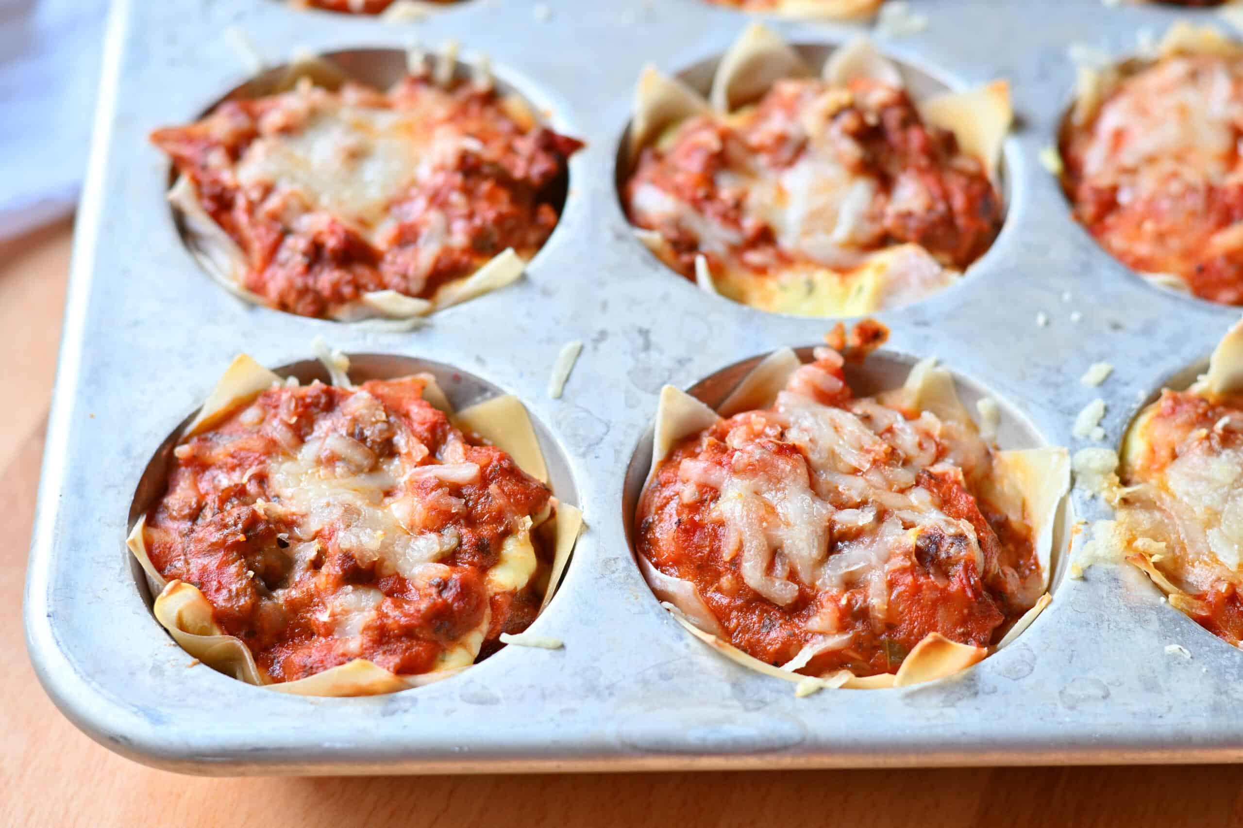 Baked lasagna cups with crisp golden untucked wonton wrapper corners standing up in a muffin tin.