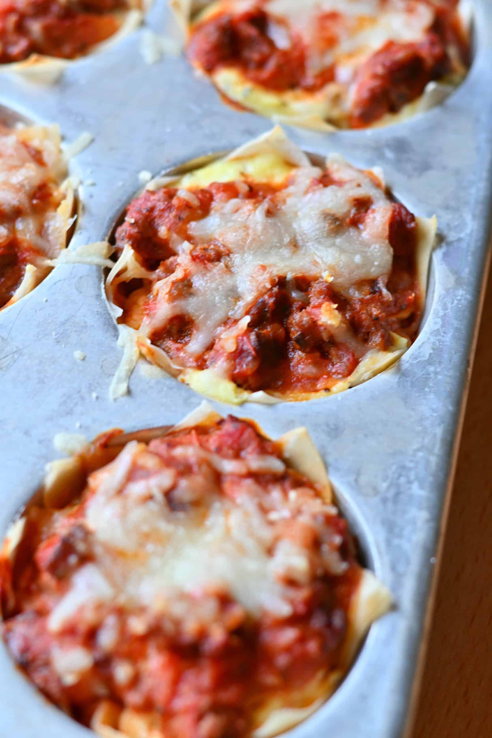 Close-up of baked lasagna cups in a muffin tin with melted cheese.